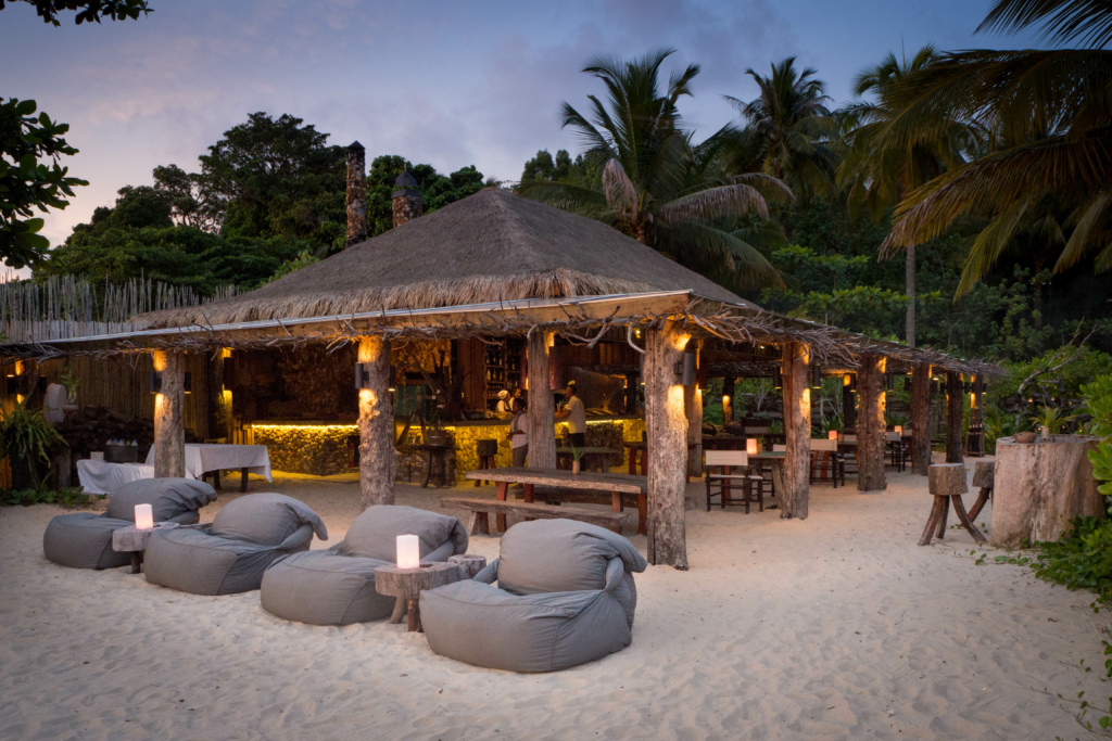 a sandy beach with lounge chairs and a thatched roof.